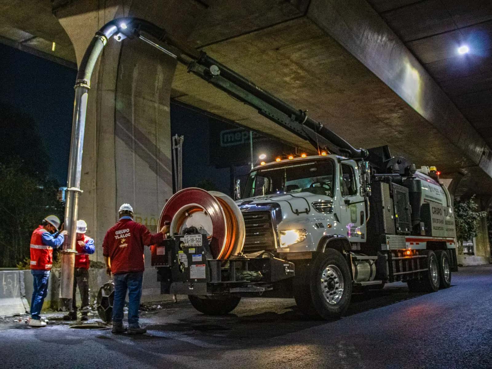 Camión de impulsión y succión con brazo de aspiración trabajando de noche bajo un puente