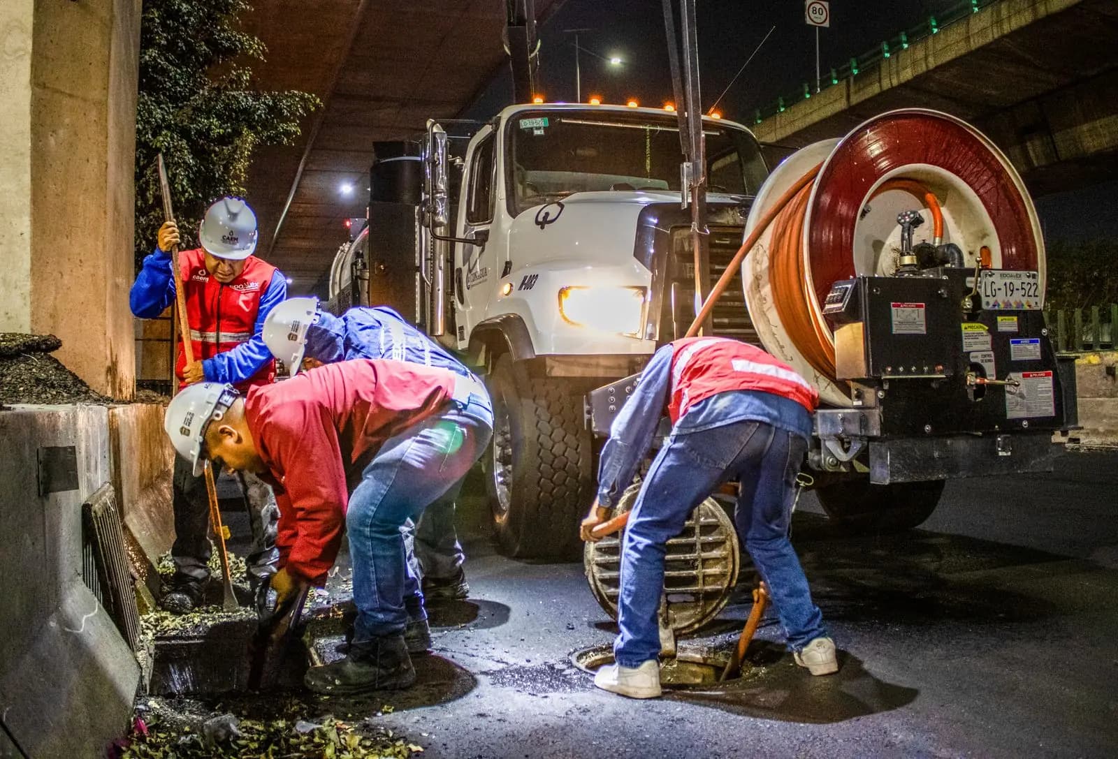 Operarios abriendo una arqueta de alcantarillado junto a un camión con carrete de manguera