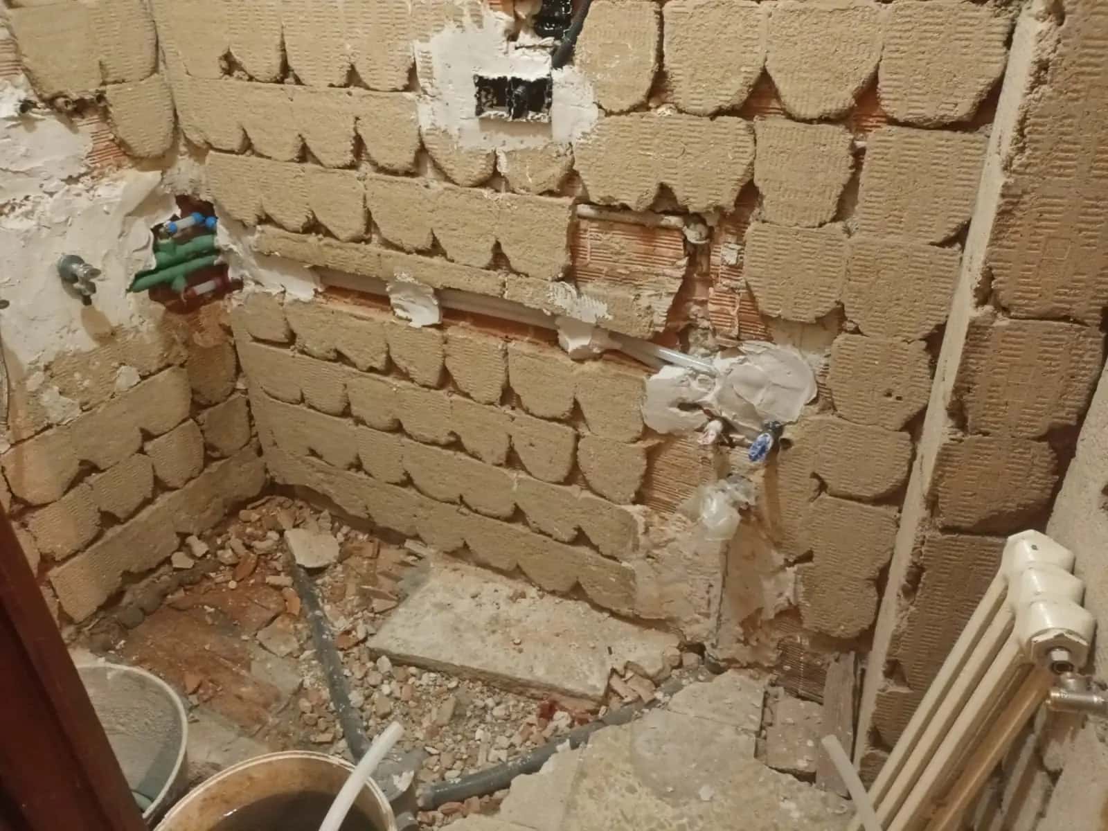 Baño demolido con paredes de ladrillo, escombros y tuberías de agua a la vista