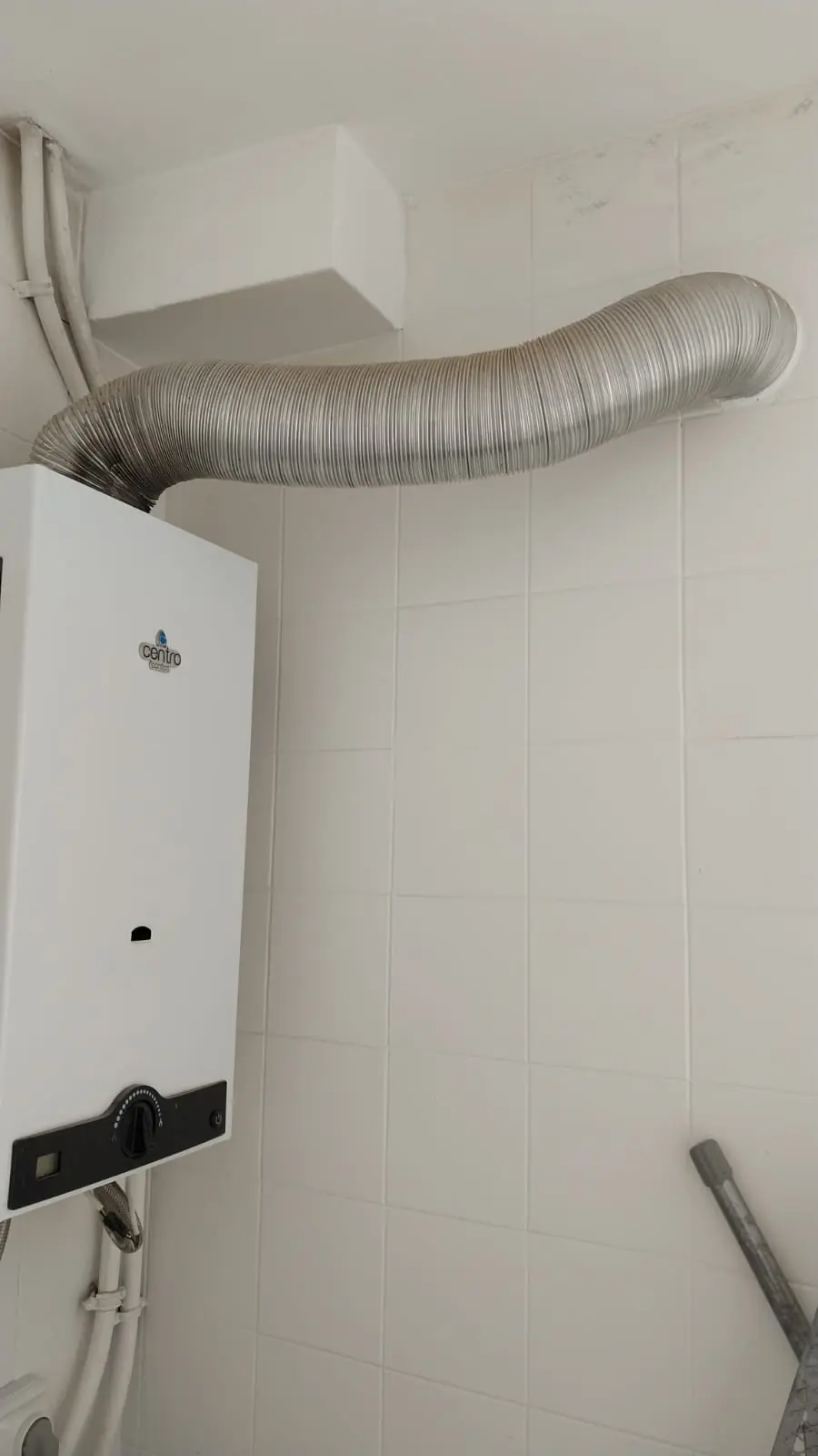 Calentador de gas blanco con tubo de salida de humos en una pared de azulejo