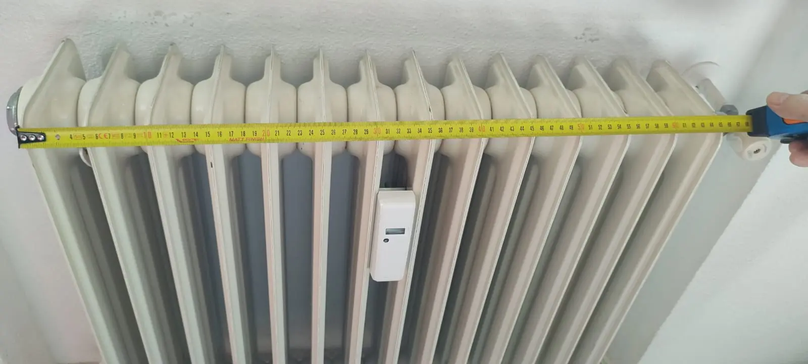 Cinta métrica midiendo el ancho de un radiador de hierro fundido