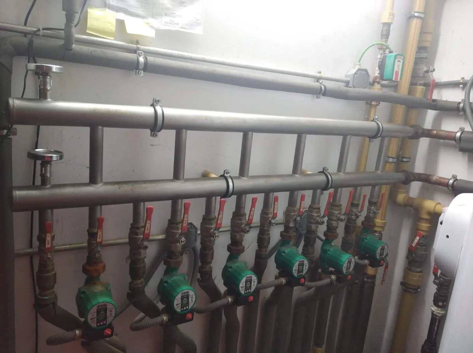 Colector de calefacción con varias bombas circuladoras verdes y llaves de corte rojas