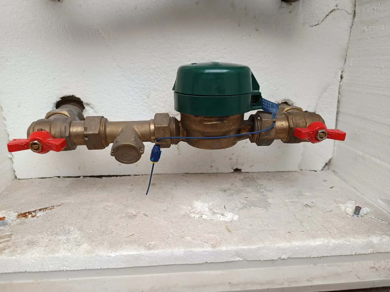 Contador de agua con llaves de corte rojas y precinto dentro de una hornacina blanca