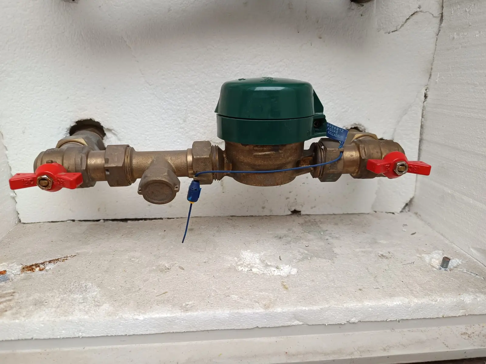 Contador de agua con llaves de corte rojas y precinto dentro de una hornacina blanca