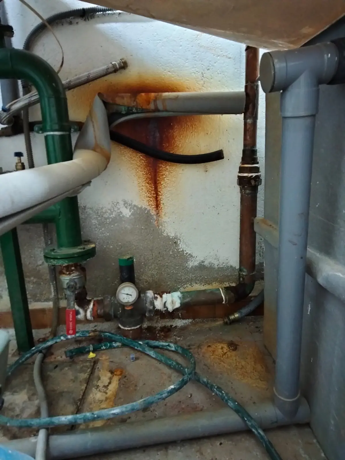 Cuarto técnico con tuberías oxidadas y regueros de óxido por goteo en la pared