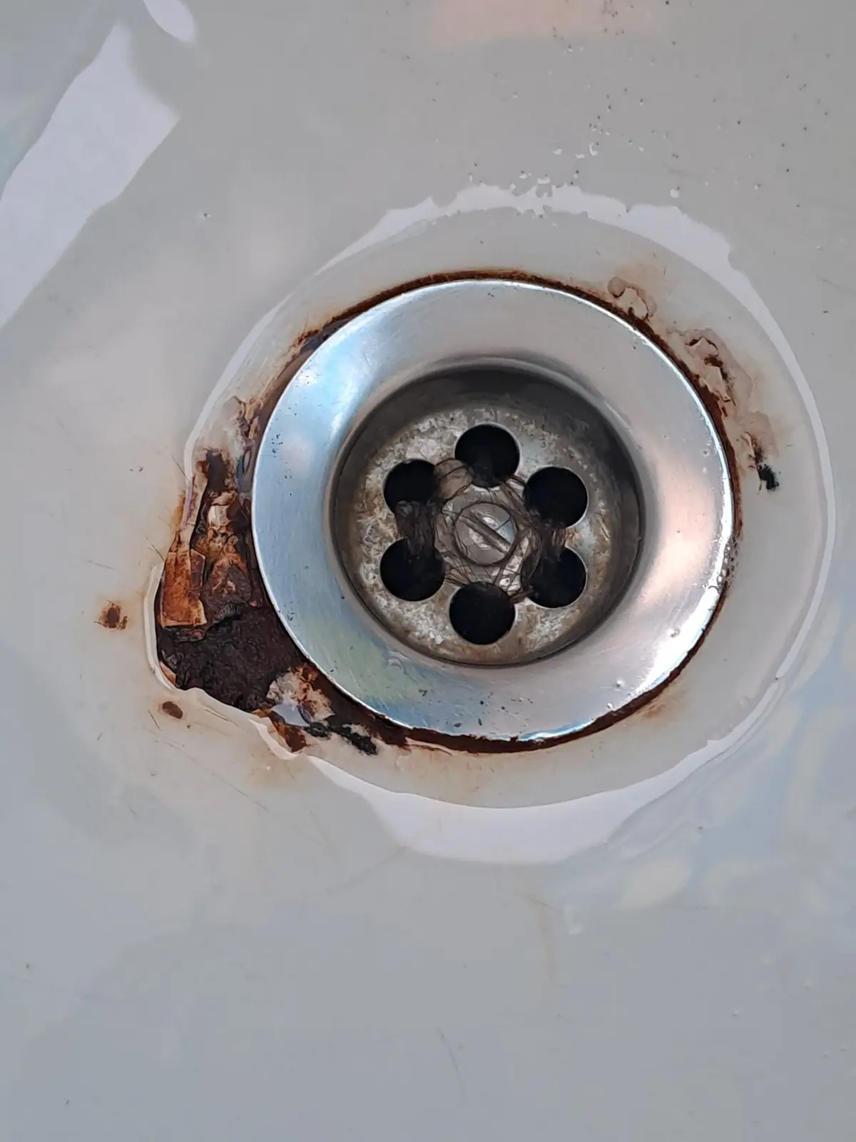 Desagüe metálico de bañera con óxido y esmalte deteriorado a su alrededor
