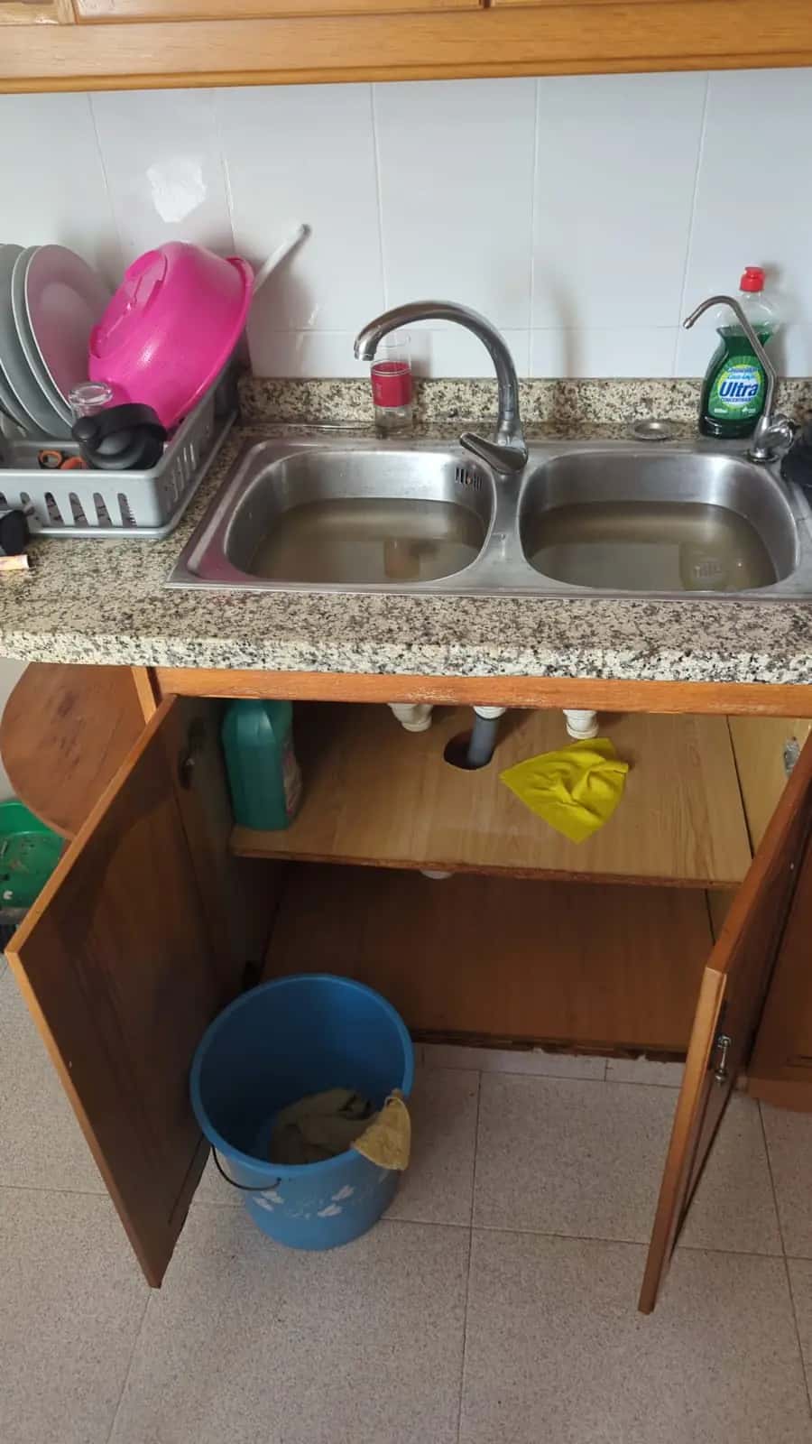 Fregadero doble de acero lleno de agua estancada con el mueble inferior abierto