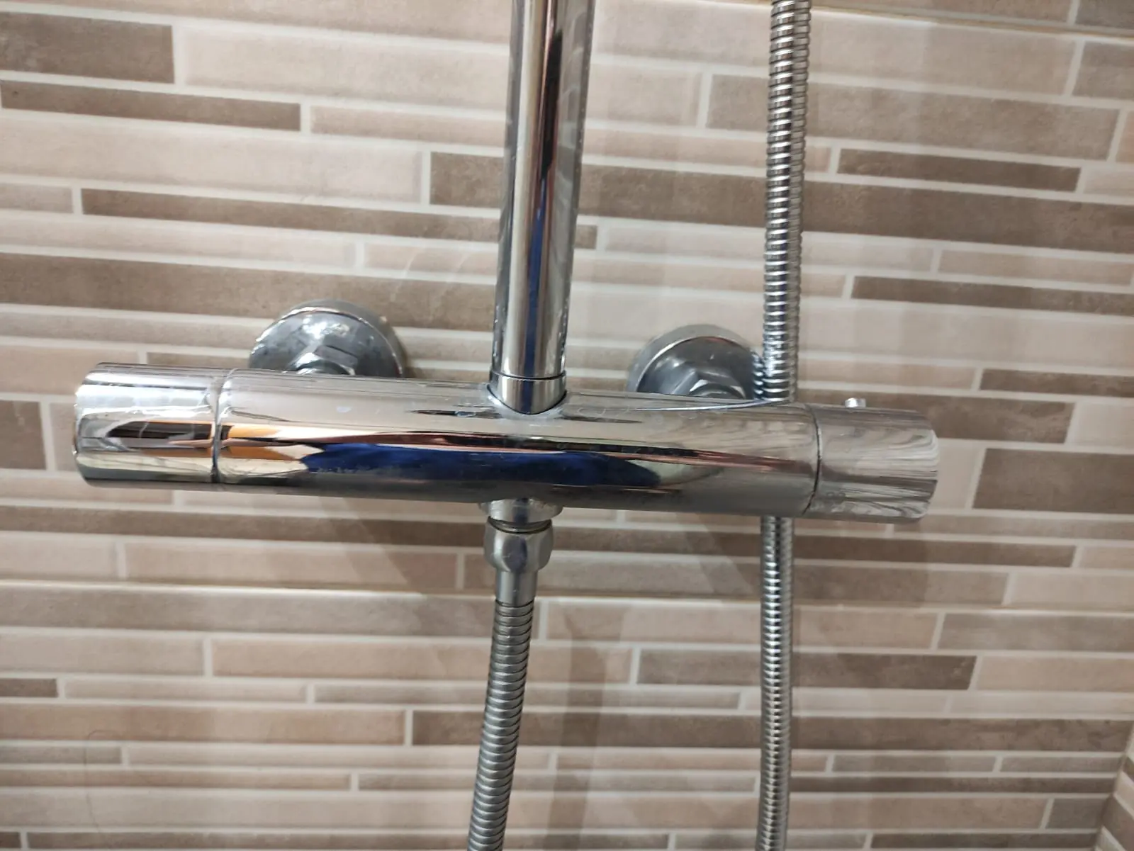 Grifo termostático cromado de ducha sobre una pared de azulejo imitación madera