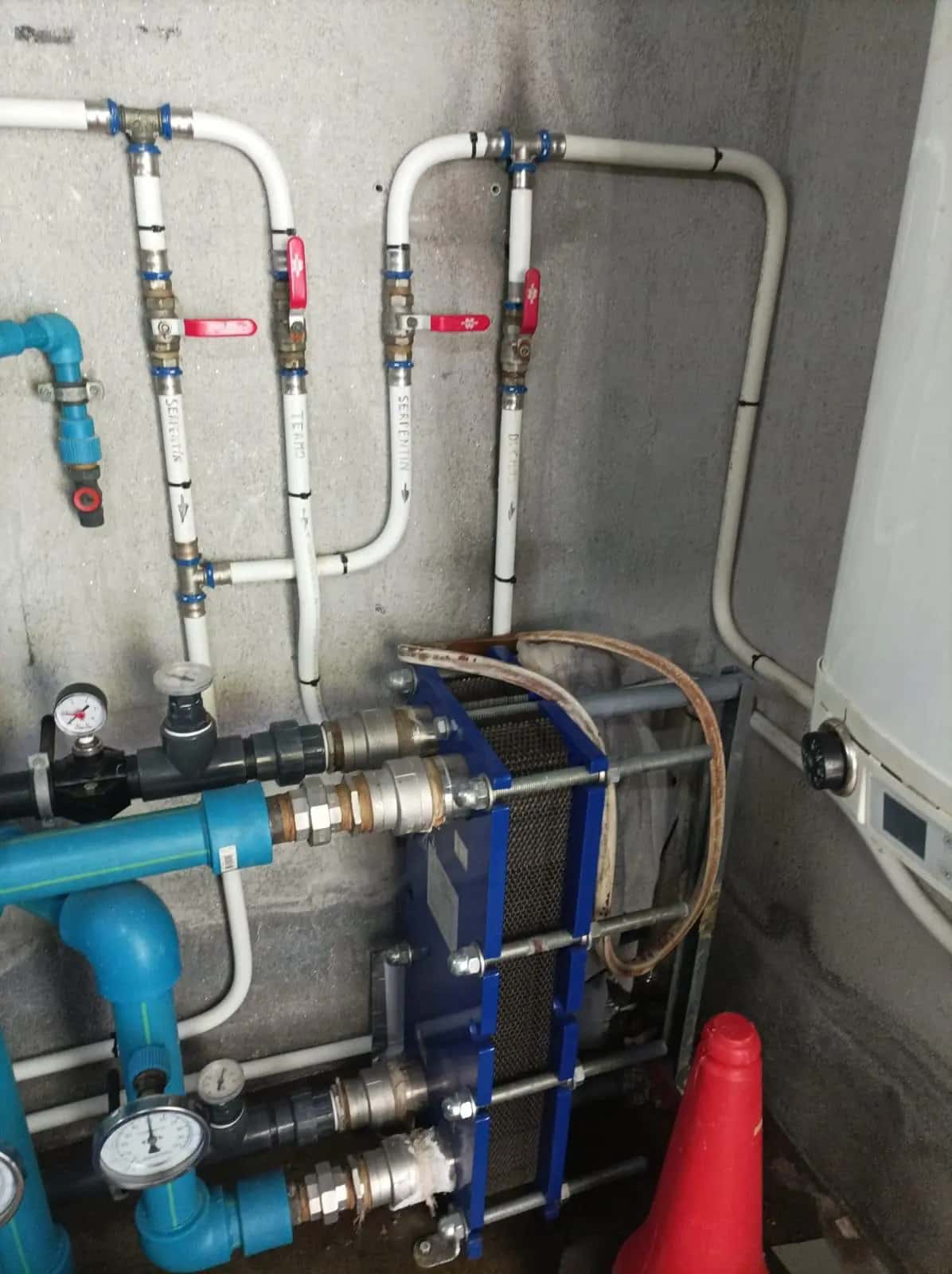 Intercambiador de placas con tuberías, manómetros y llaves de corte en un cuarto técnico
