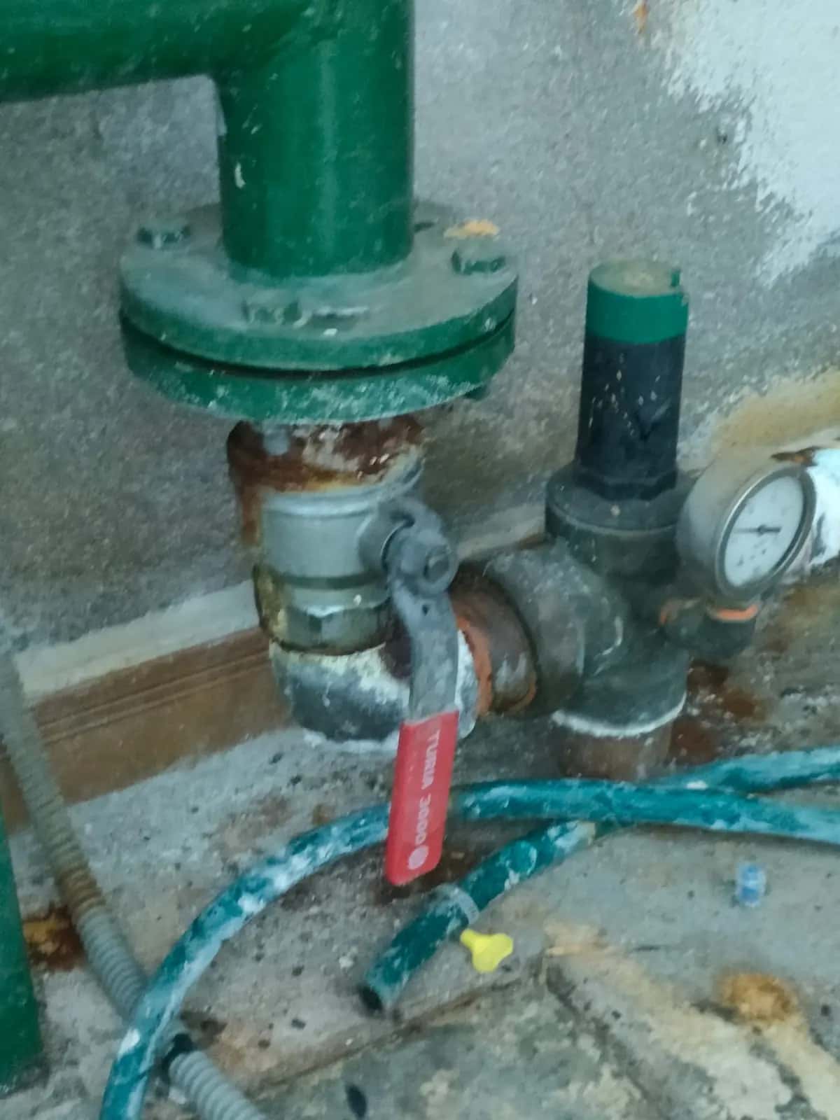 Llave de corte oxidada y válvula reductora con manómetro en un cuarto de contadores