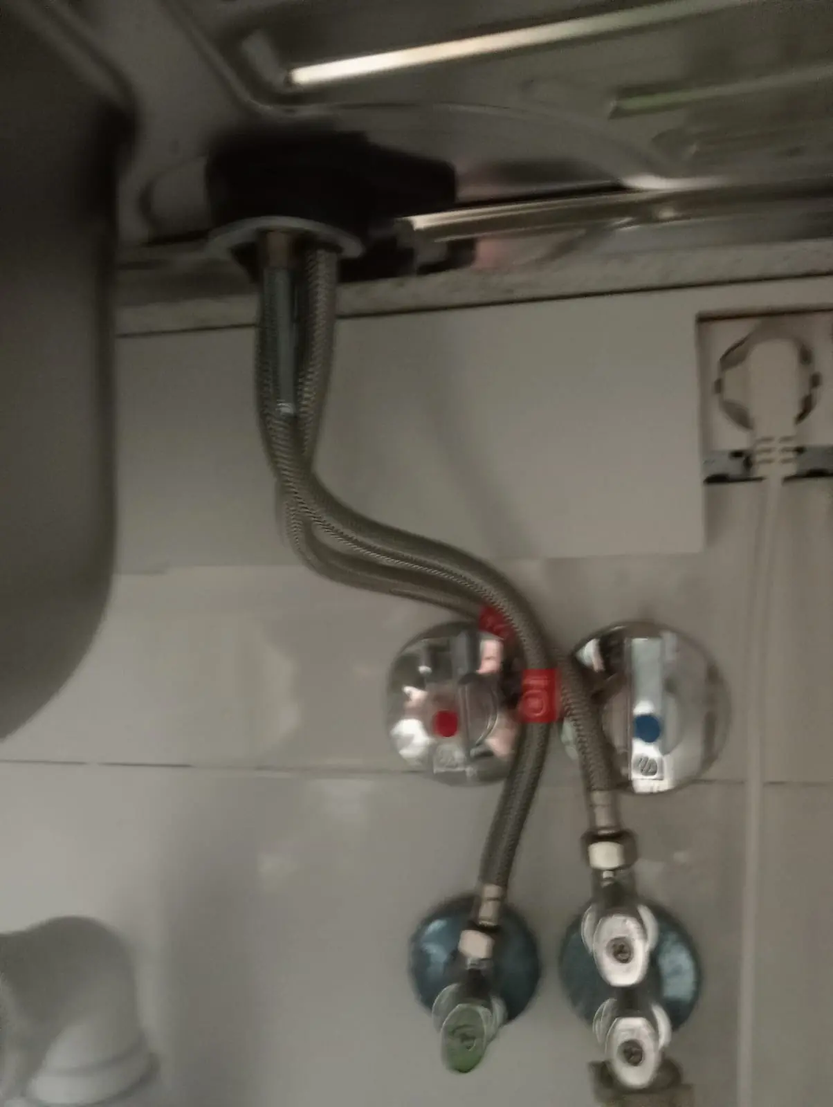 Llaves de escuadra con latiguillos metálicos bajo un fregadero de cocina