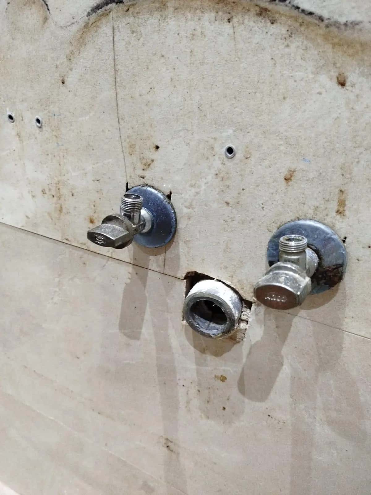 Llaves de escuadra y salida de desagüe en una pared de azulejo con manchas