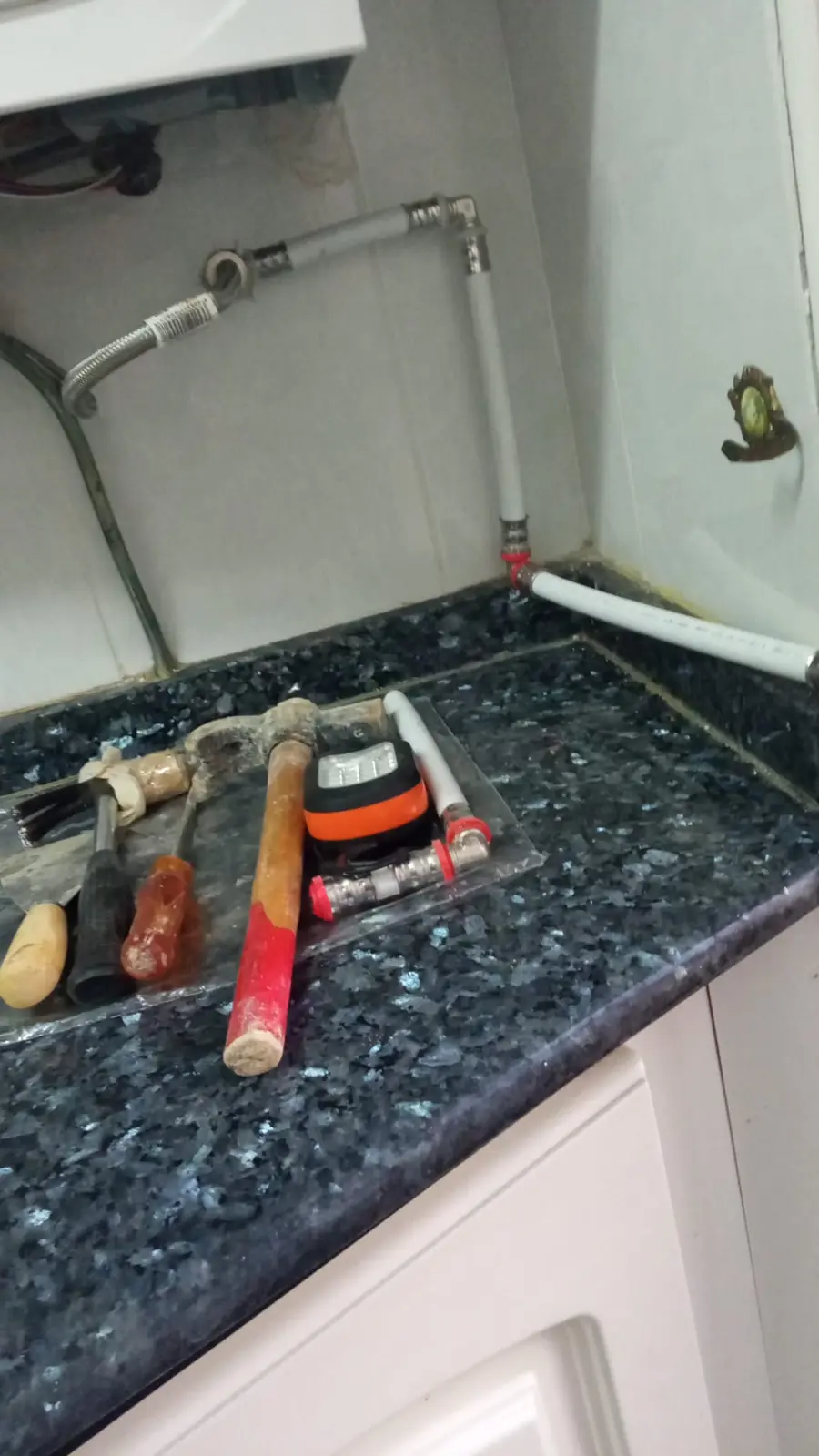 Martillo, cinceles y tubería nueva sobre una encimera junto a una instalación de agua