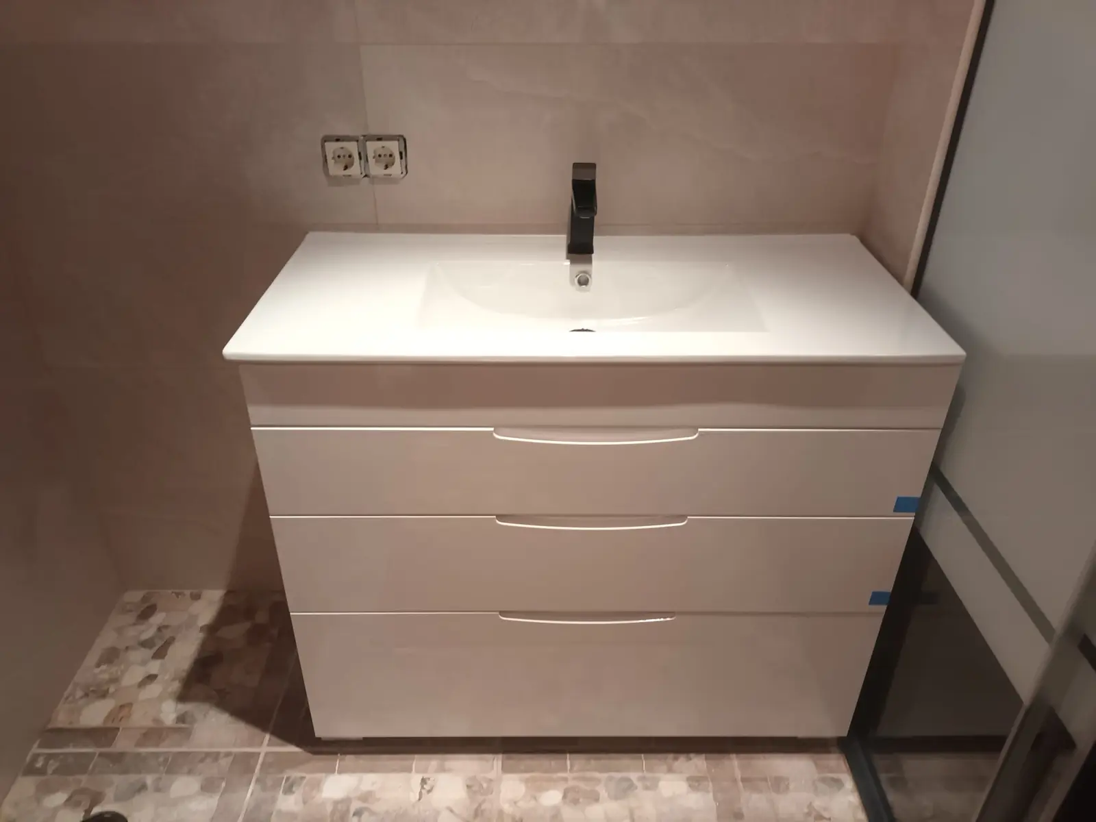 Mueble de lavabo blanco con grifo negro en un baño con suelo de piedra