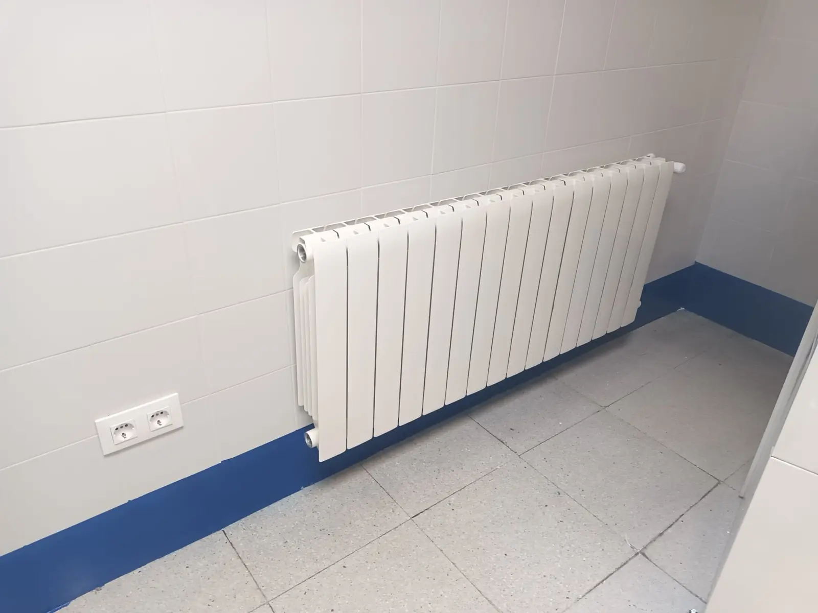 Radiador de aluminio blanco instalado en una pared de azulejo con zócalo azul