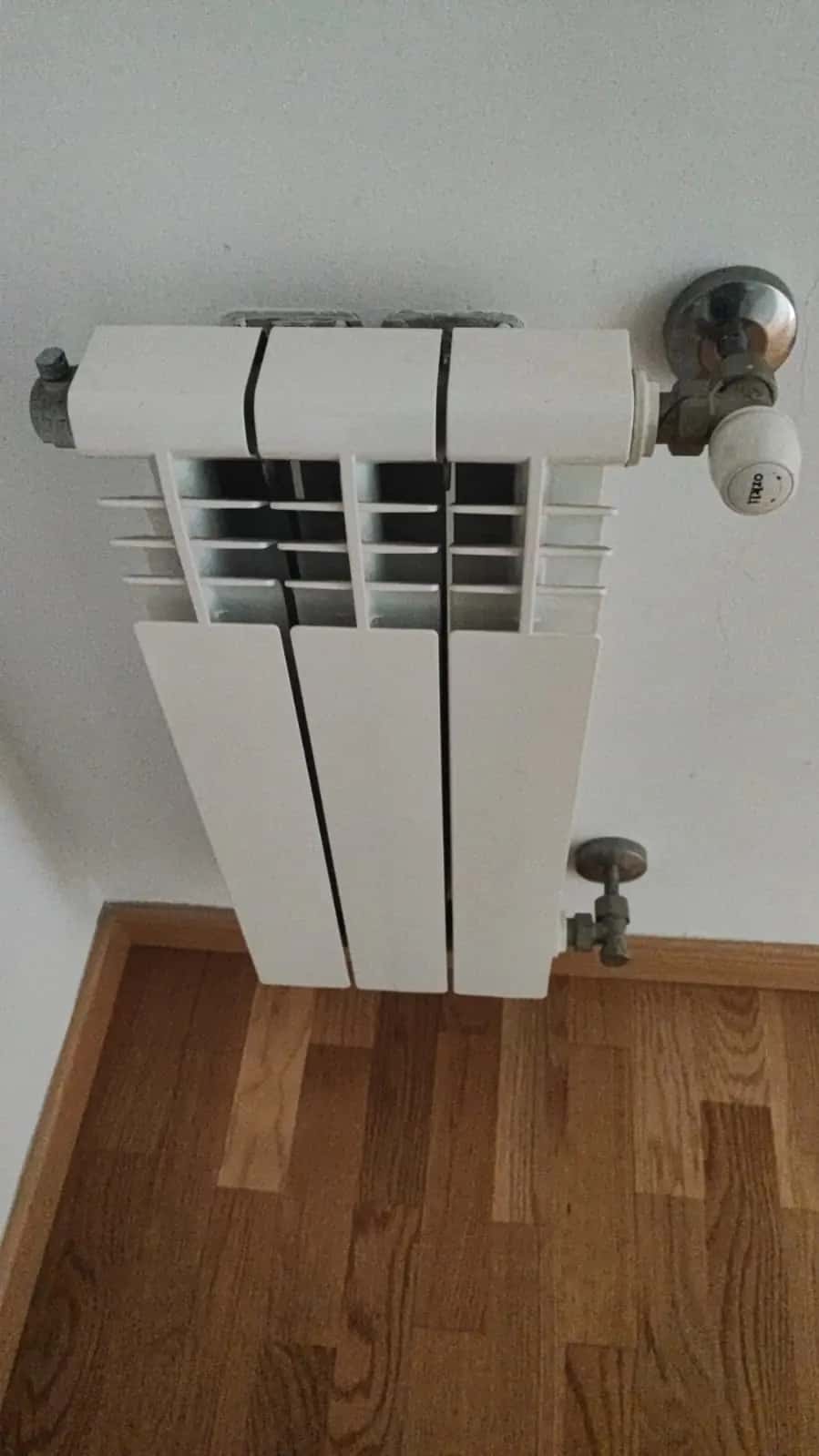 Radiador blanco con válvula termostática instalado sobre un suelo de parquet