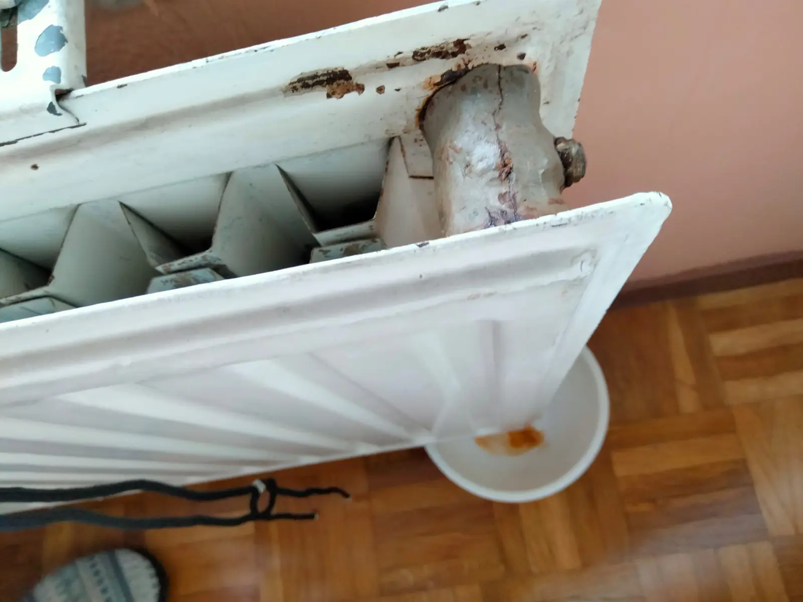 Radiador desmontado con agua oxidada goteando en un recipiente sobre el parquet