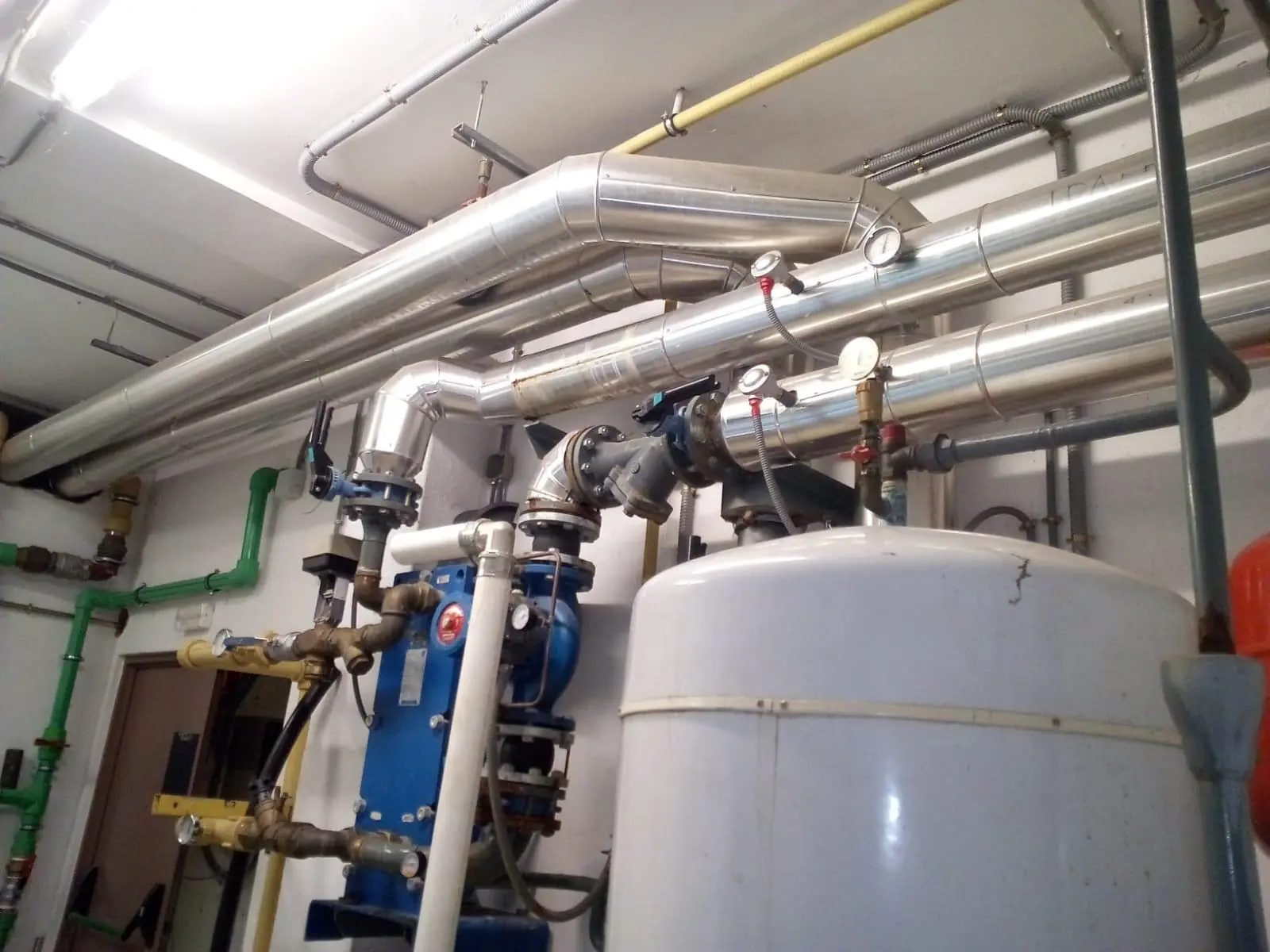 Sala de máquinas con depósito acumulador, intercambiador y tuberías aisladas junto al techo
