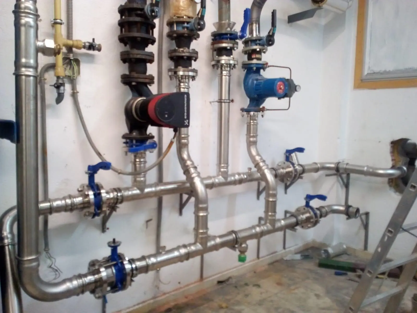 Sala técnica con tuberías de acero inoxidable, bombas de circulación y llaves azules