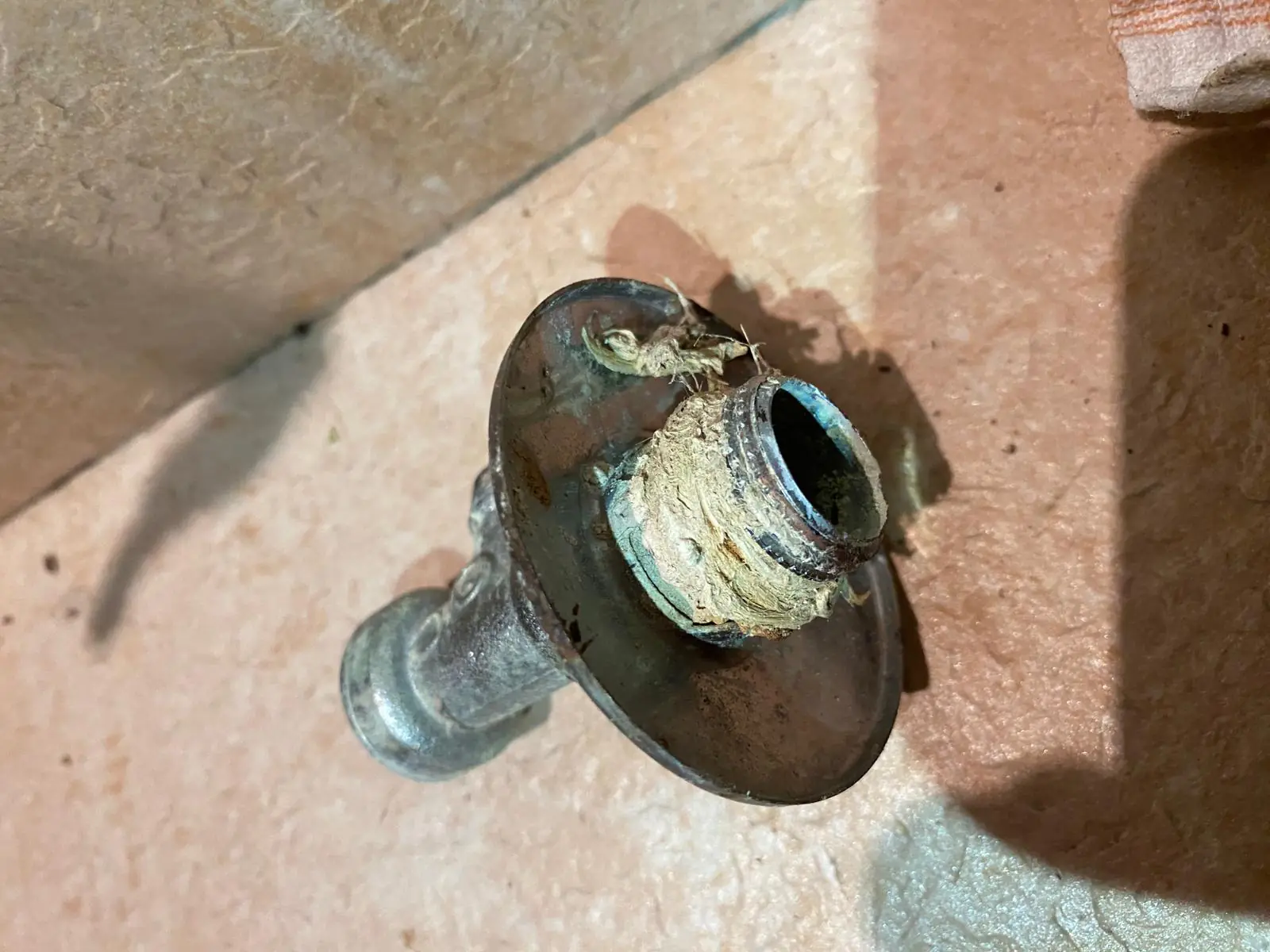 Salida de tubería corroída con restos de cáñamo en la rosca sobre suelo de obra
