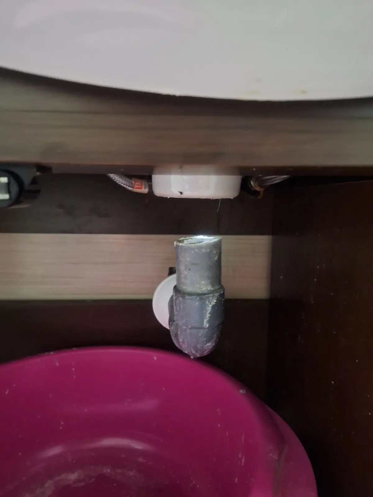 Sifón bajo un lavabo con gotas de agua cayendo sobre un barreño rosa