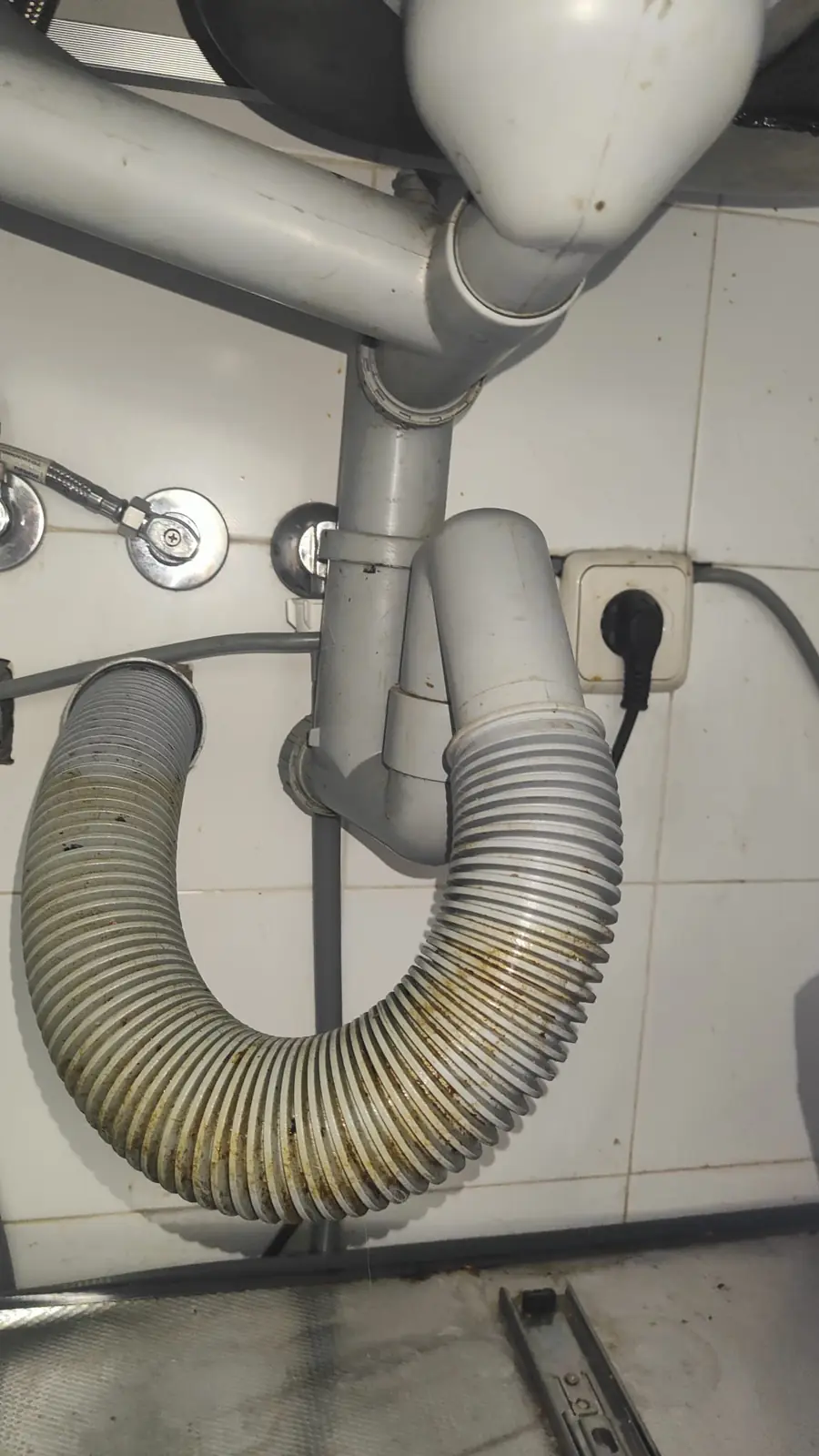 Sifón de PVC y tubo corrugado sucio de desagüe bajo un fregadero de cocina