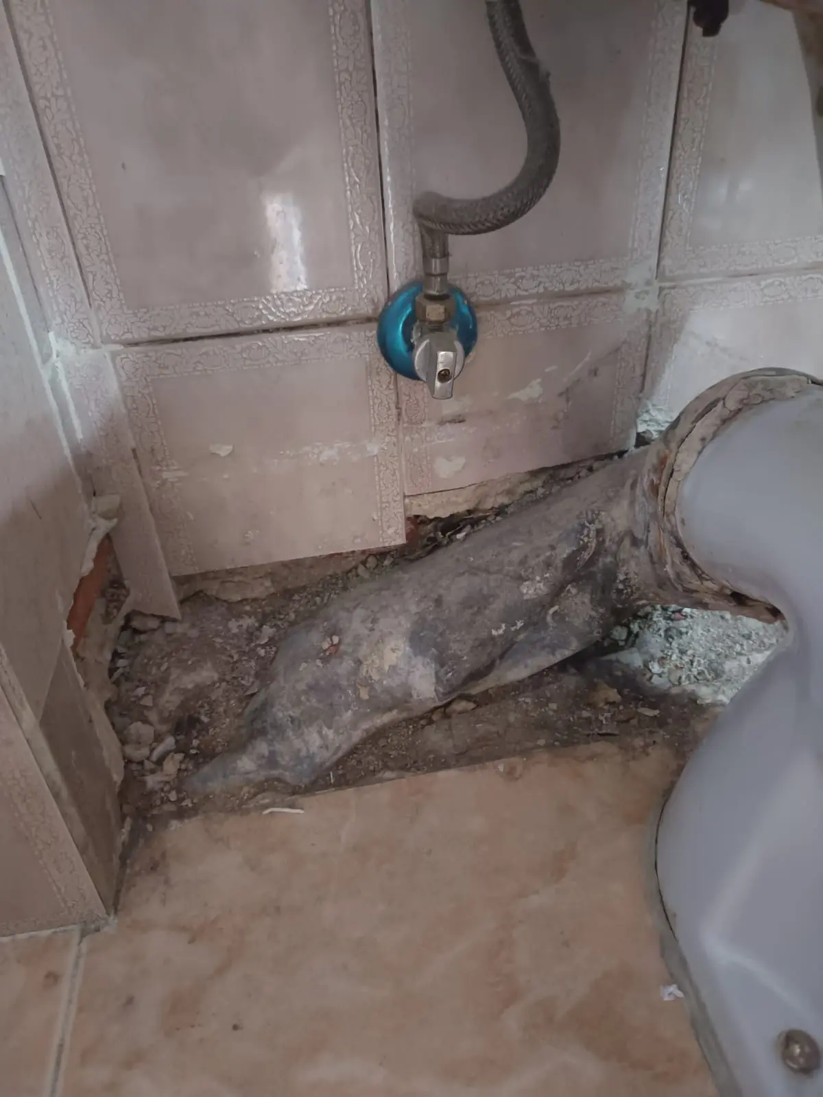 Suelo roto junto a un inodoro que deja a la vista una tubería de desagüe antigua