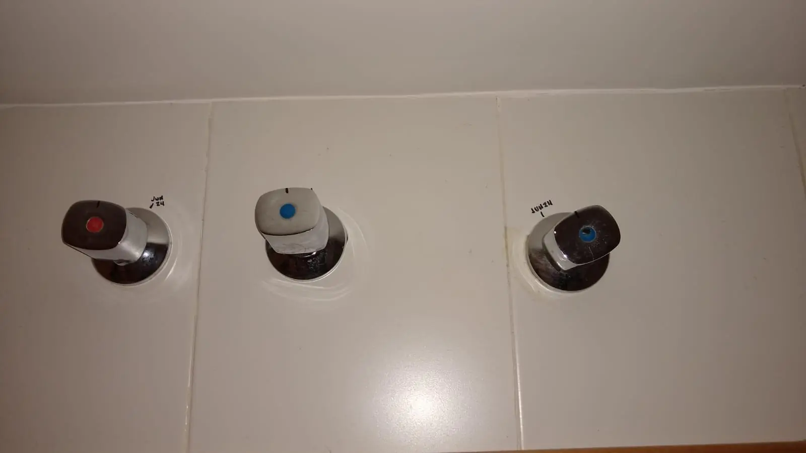 Tres llaves de paso empotradas en una pared de azulejo blanco
