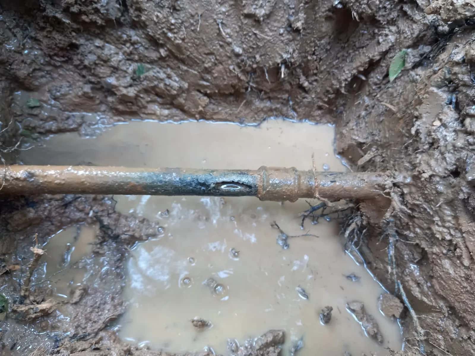 Tubería enterrada con una fuga de agua en una zanja embarrada y encharcada