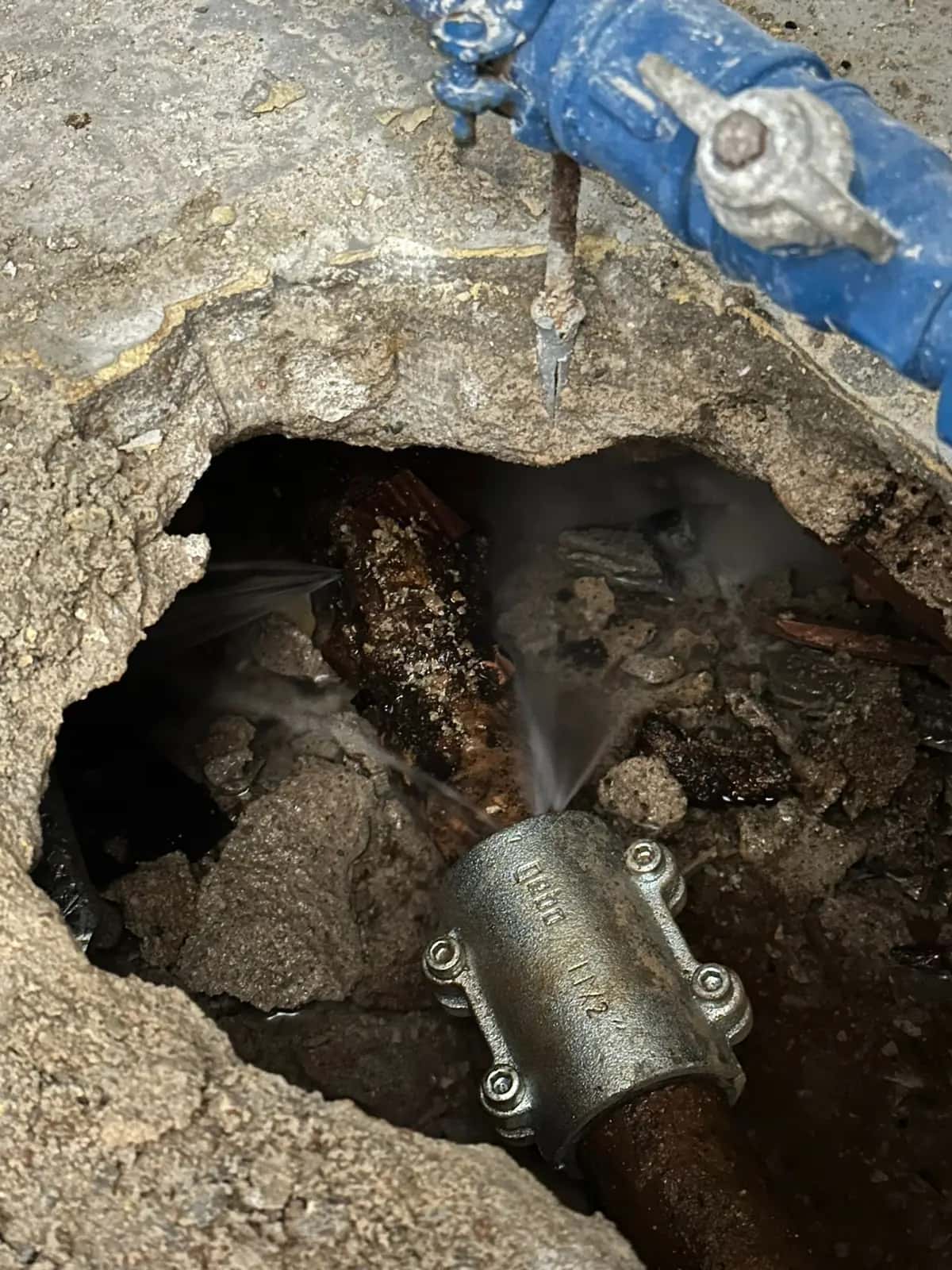 Tubería rota que pierde agua a presión dentro de un agujero junto a una abrazadera