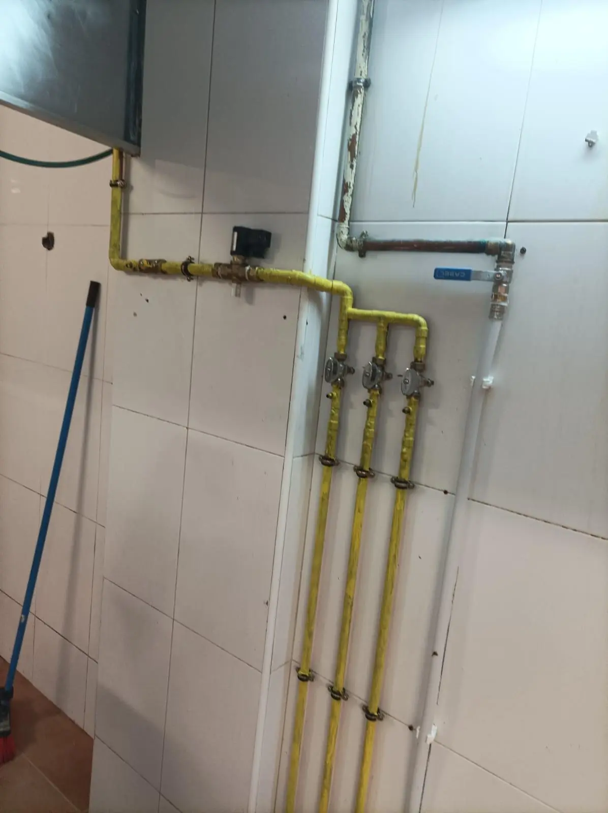 Tuberías amarillas de gas con llaves de corte sobre una pared de azulejo blanco