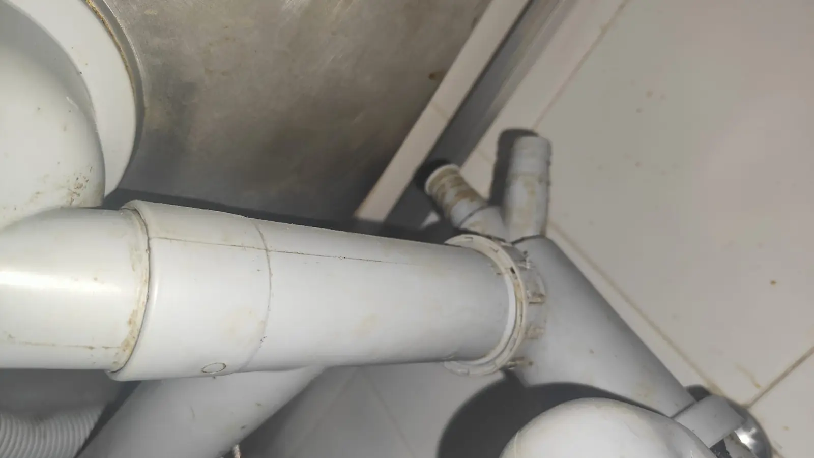 Tuberías de desagüe de PVC gris con derivaciones y abrazaderas bajo un fregadero