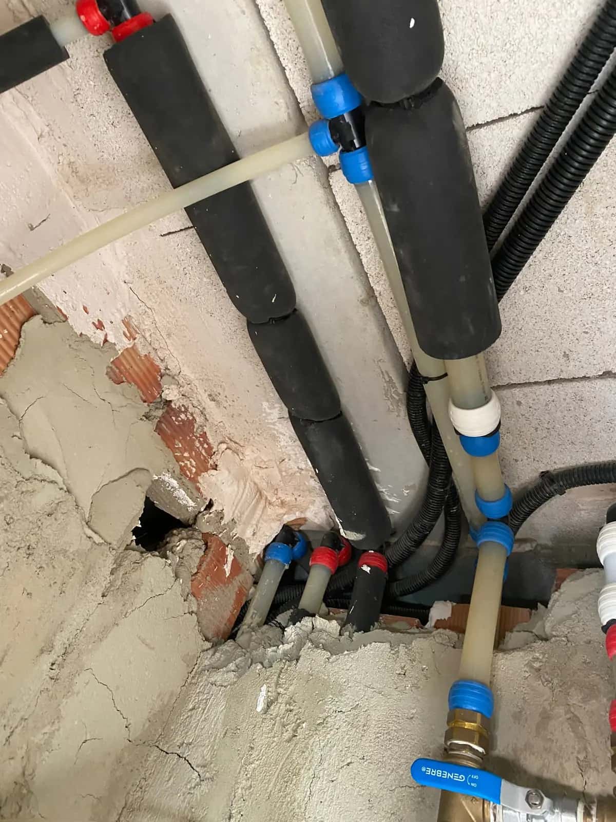 Tuberías multicapa con aislamiento negro y llave de paso en una pared abierta