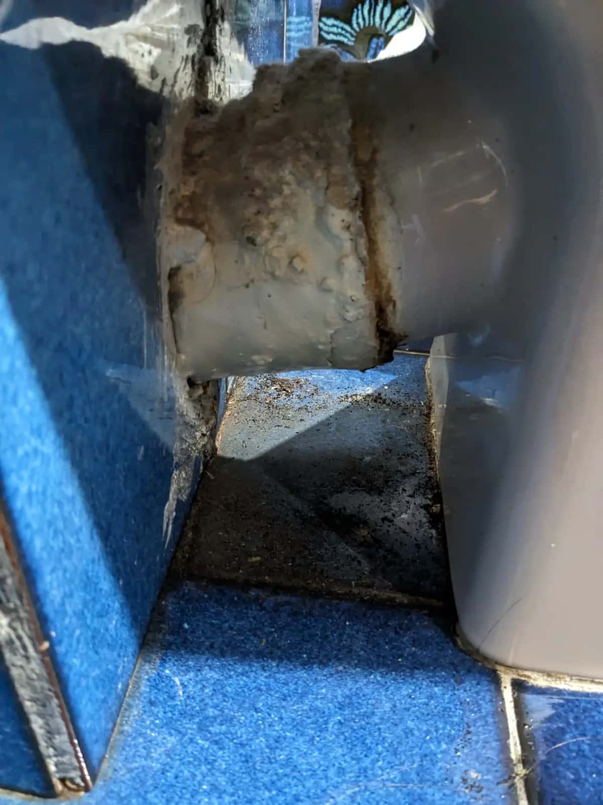 Unión de tubería de desagüe con incrustaciones y suciedad entre azulejos azules